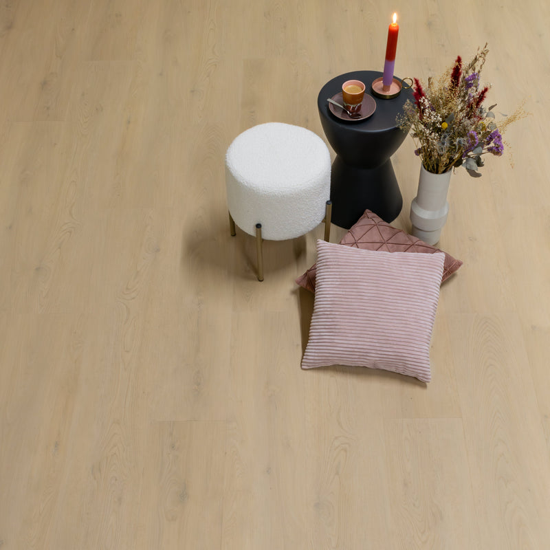 licht beige eiken vloer met fijne, natuurlijke houtnerf en knoestpatroon, brede planken, matte afwerking, gestyled met wit bouclé krukje, zwart bijzettafeltje met multicolor rode naar paars verlopende kaars, kopje koffie op paars schoteltje en vaas met droogboeket naast twee zachte kussens in pastelroze tinten