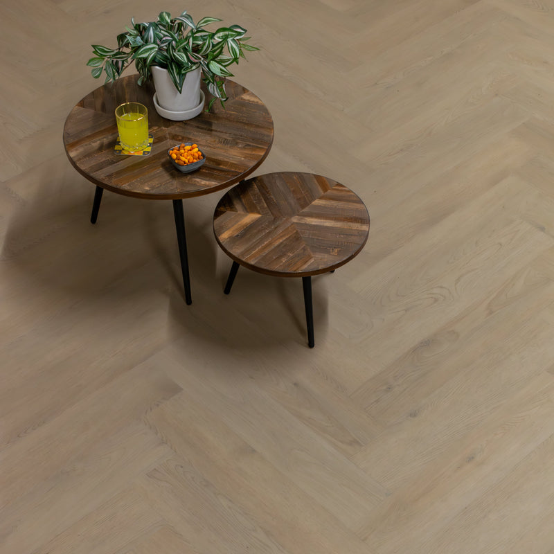 lichte vloer met visgraatpatroon in licht beige eiken met subtiele houtstructuur, houten ronde bijzettafels met diagonale latten en een groene kamerplant op de grote tafel
