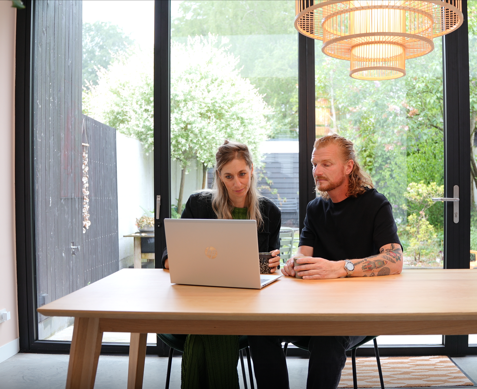 Tafelblad van licht eiken hout met een natuurlijke houtnerf, onder een warme hanglamp met ronde houten details, in een lichte, moderne woonkameromgeving.