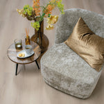 Lichte eiken vloer met matte afwerking en natuurlijke houtstructuur in brede planken gelegd, sfeervol interieur met grijs velours fauteuil en een tafeltje met decoratie en bloemenvaas.
