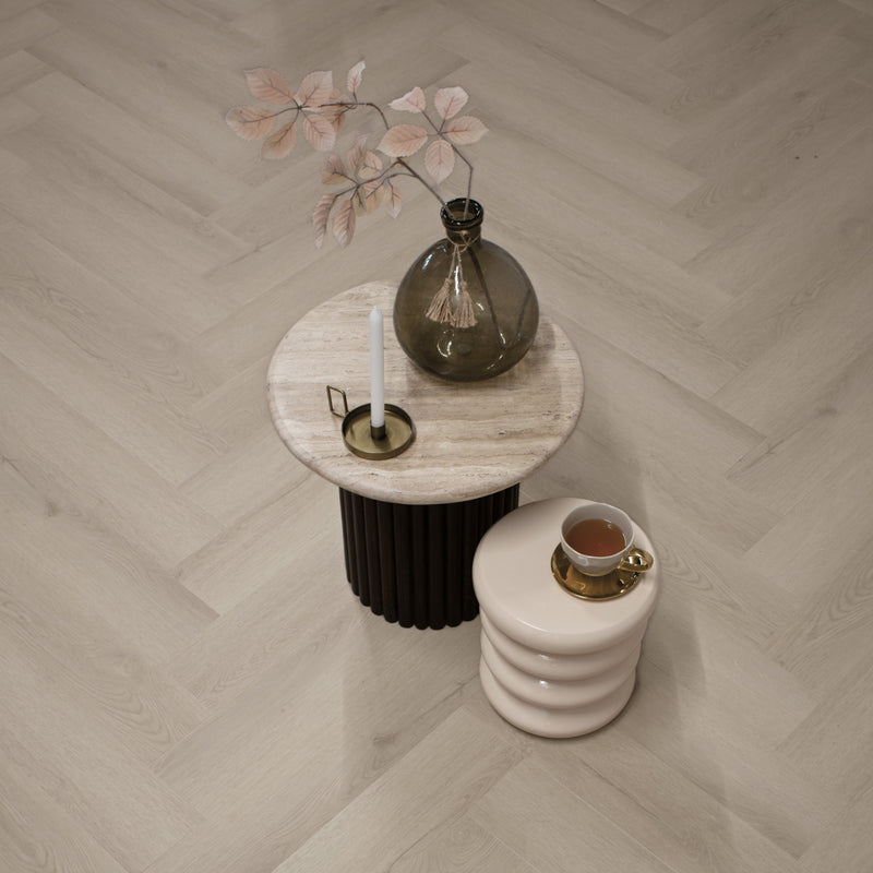licht eiken visgraatvloer met natuurlijke houtstructuur en brede planken, lichte beige ondertoon, gecombineerd met ronde stenen bijzettafel met glazen vaas en witte kaars