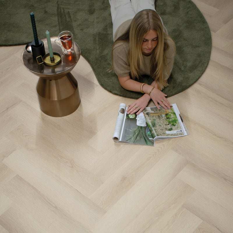 licht eiken visgraatvloer met fijne houtstructuur gecombineerd met groen rond vloerkleed en metalen bijzettafel met kaarsen en glazen theekopje
