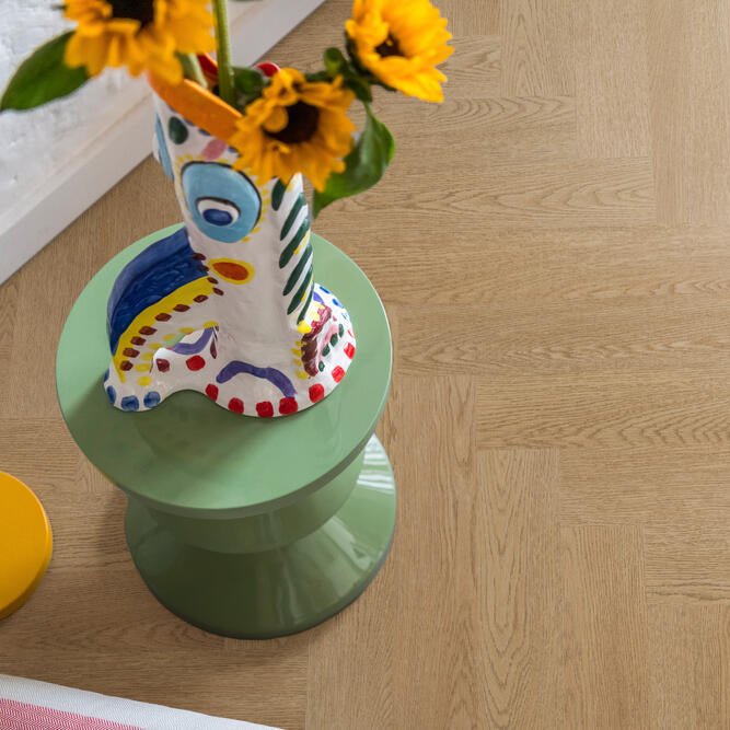 licht eiken vloer in visgraatpatroon met lichte houtstructuur, groene bijzettafel met kleurrijke vaas en gele zonnebloemen erop
