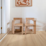 lichte beige eiken vloer met brede planken en rechte nerfstructuur, twee minimalistische houten stoelen met robuuste rechte lijnen tegen een witte muur, abstracte oranje kunst aan de muur