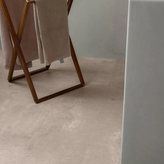 lichte beige tegelvloer met subtiele, vloeiende streken en matte structuur, gecombineerd met een bruine houten kledingstandaard met zachte beige stoffen doeken