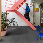 donkergrijze tegelvloer met grote matte tegels met subtiel golvend streeppatroon in een moderne woonkamer met een roze trap en blauwe stoel