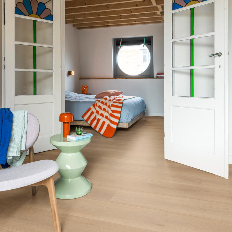 lichte beige eiken vloer met brede planken met subtiele structuur in modern ingerichte slaapkamer met witte binnendeuren met gekleurd glas in lood, lichtgroene bijzettafel en oranje accenten zoals een lampje en deken